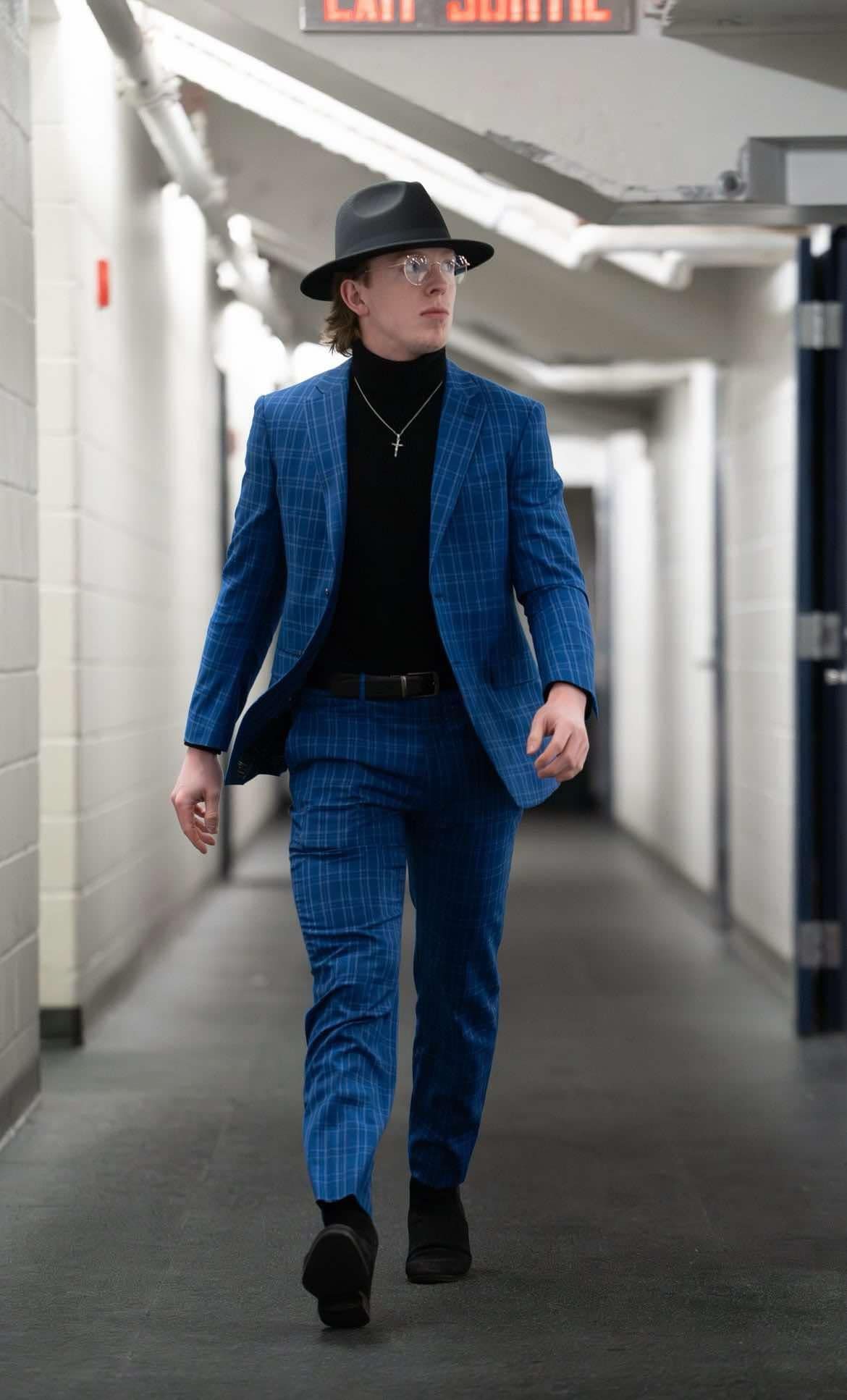 A man in a blue suit and hat is walking down a hallway.