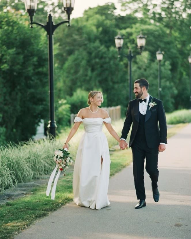 A bride and groom are walking down a path holding hands.