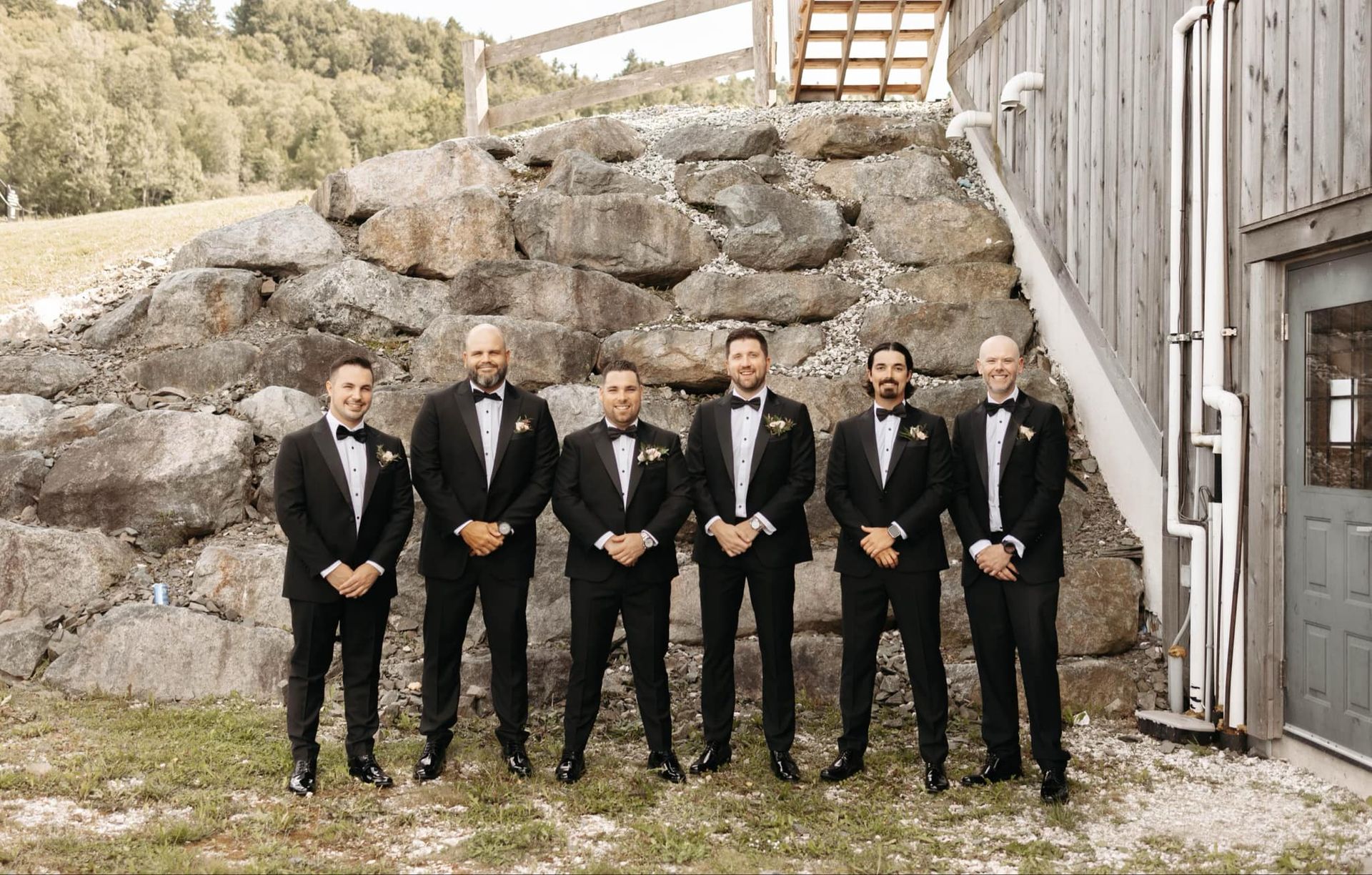 The groom and his groomsmen are posing for a picture in front of a stone wall.