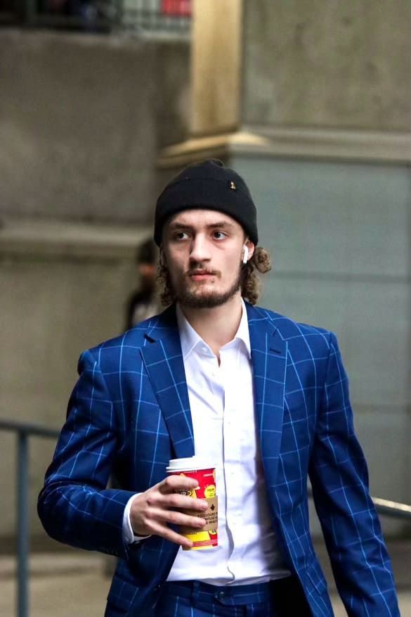 A man in a suit and beanie is holding a cup of coffee.