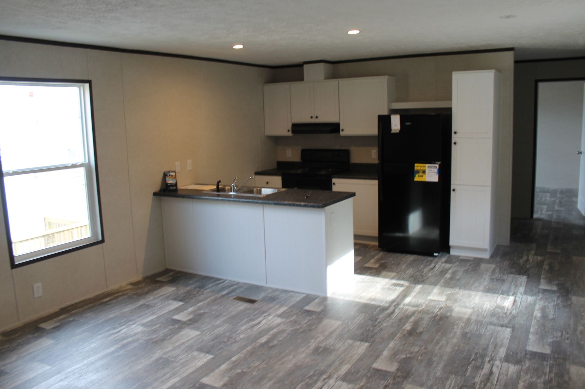An empty kitchen with a black refrigerator and white cabinets