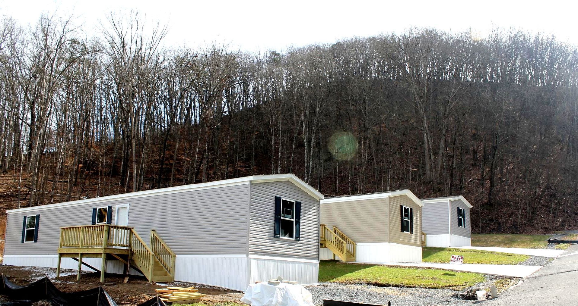 A mobile home with a deck is sitting in the middle of a grassy field.