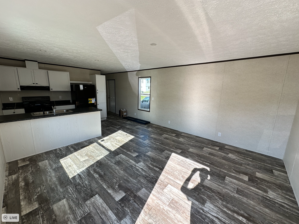 An empty living room with a kitchen in the background.