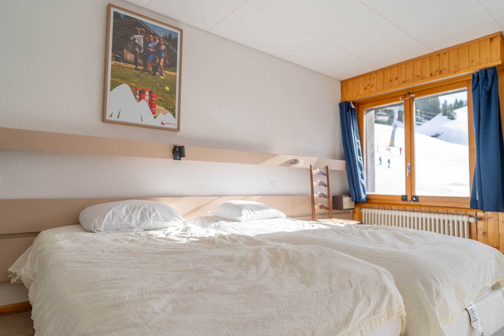 Bedroom with two beds, a framed photo, and a window overlooking snow-covered landscape.