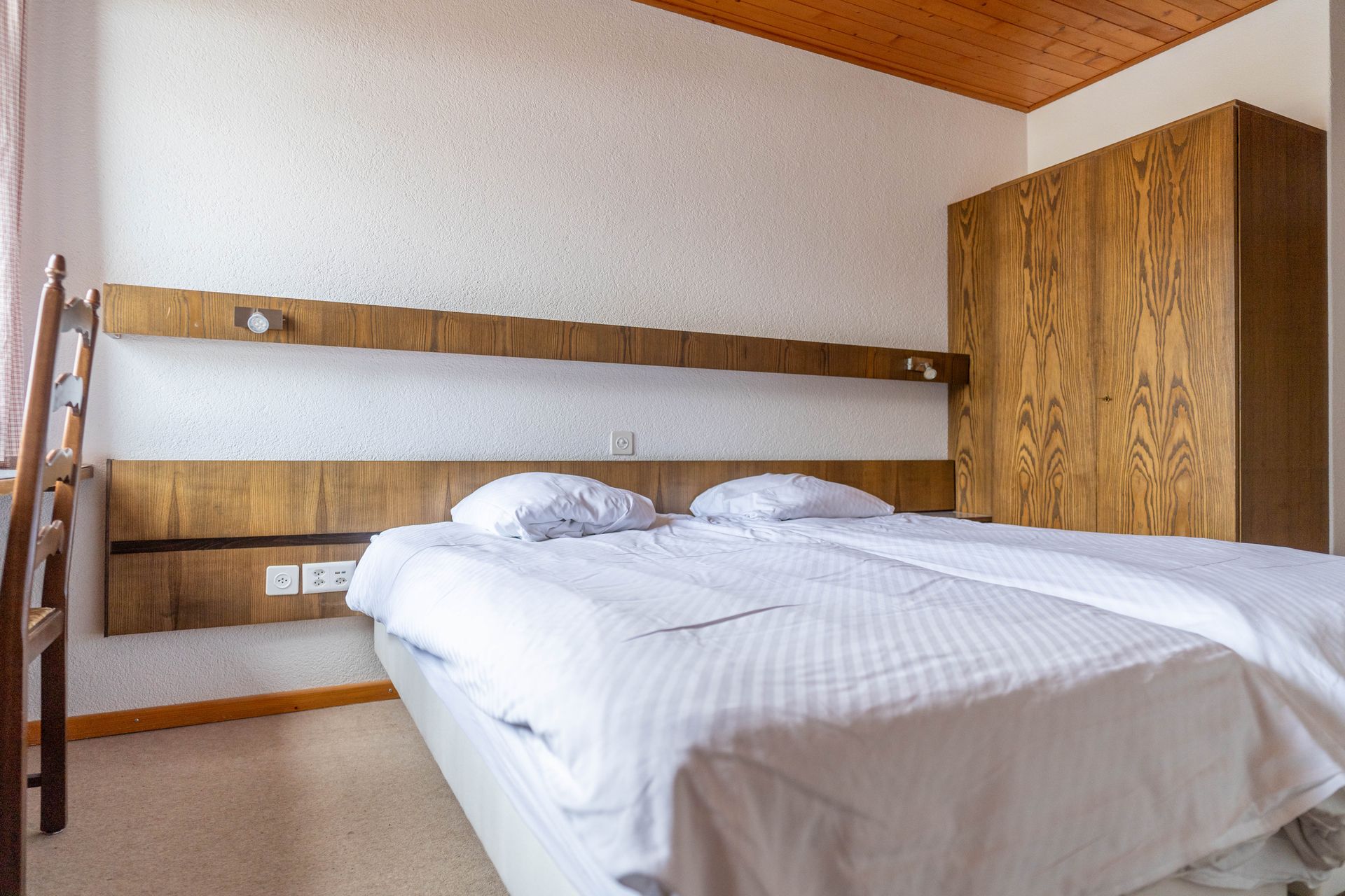 Cosy bedroom with wooden paneling, a bed, and a window overlooking a snowy mountain.