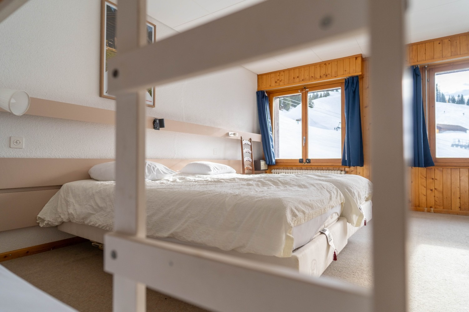Bedroom with a white bed, wooden accents, and a snow-covered mountain view.