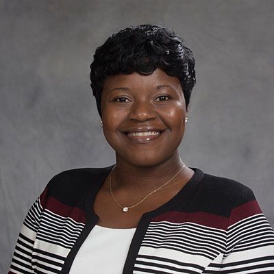 Woman with short, dark hair, smiling, wearing a black, white, and burgundy striped cardigan over a white top.