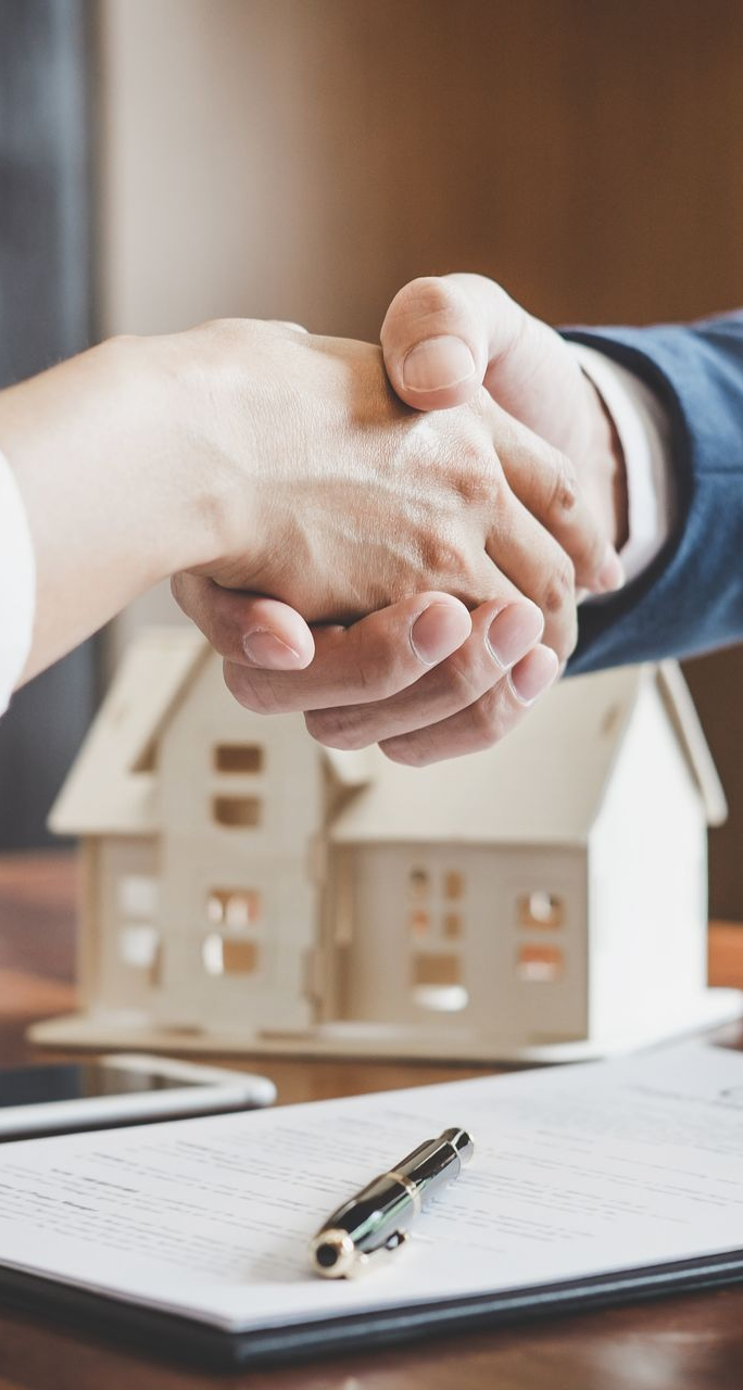 People shaking hands over a property contract and a miniature house model.