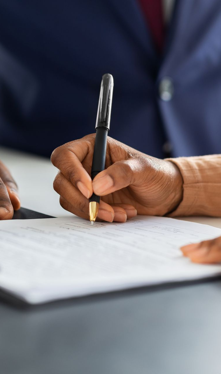 Person signing a document with a pen, close-up.