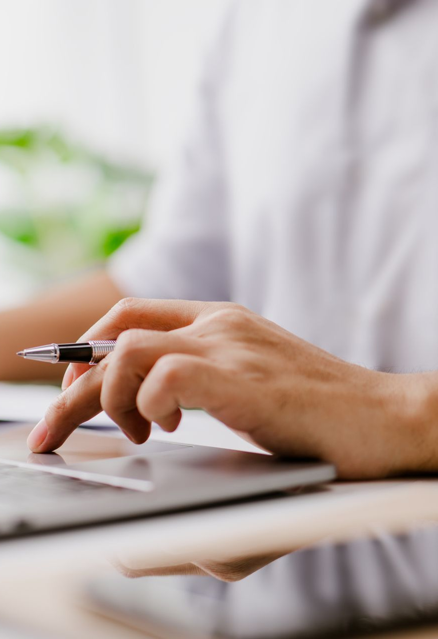 Person's hand using a pen while resting a finger on a laptop's touchpad.