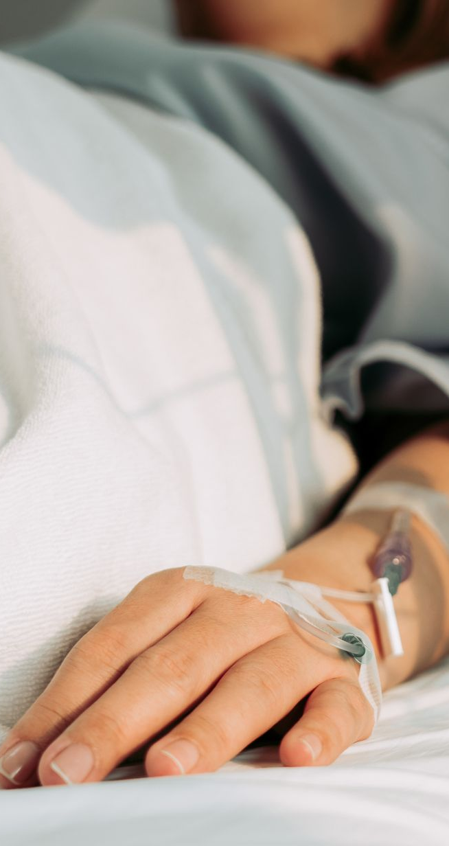 Person's arm with IV line in hospital bed.