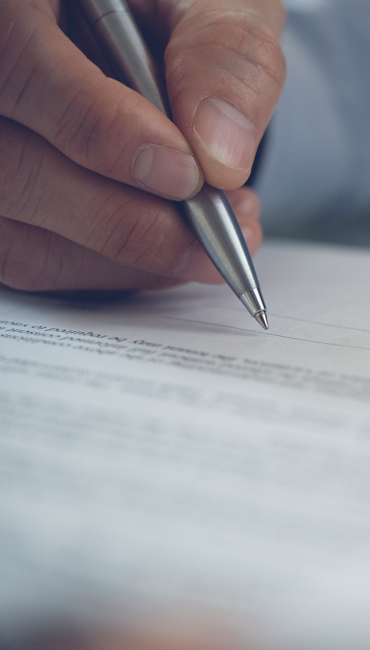 Hand holding a silver pen, writing on a document.