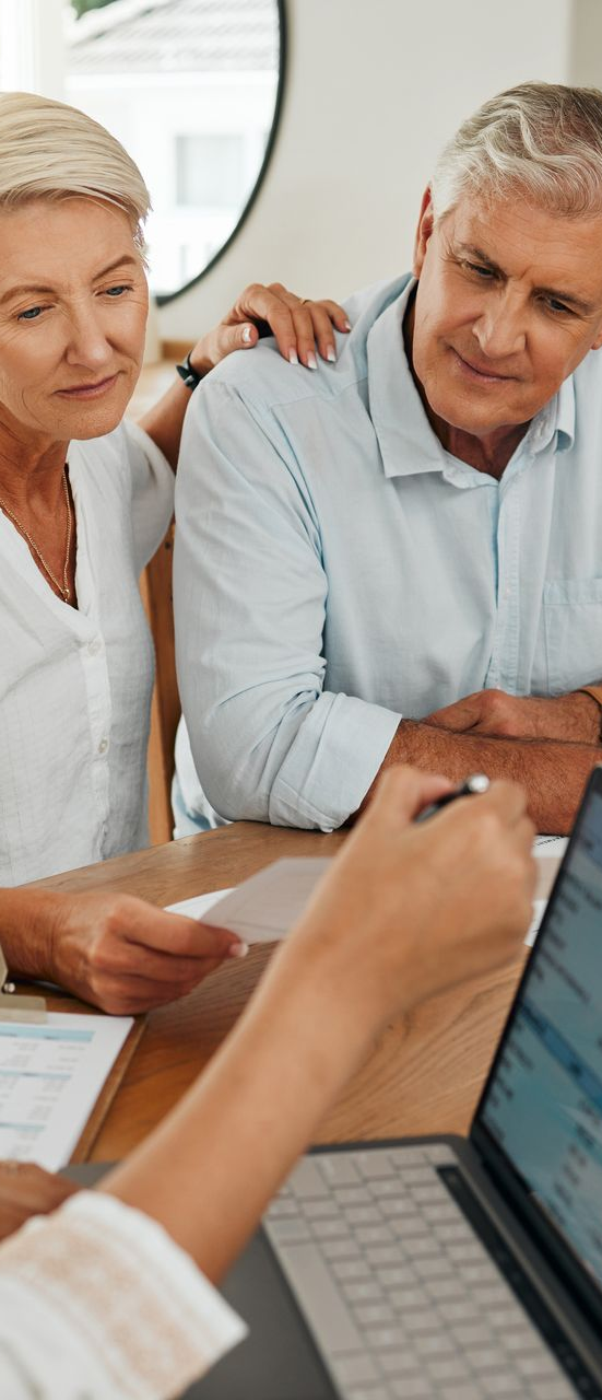 A couple reviewing documents with someone pointing at a laptop, indoors.