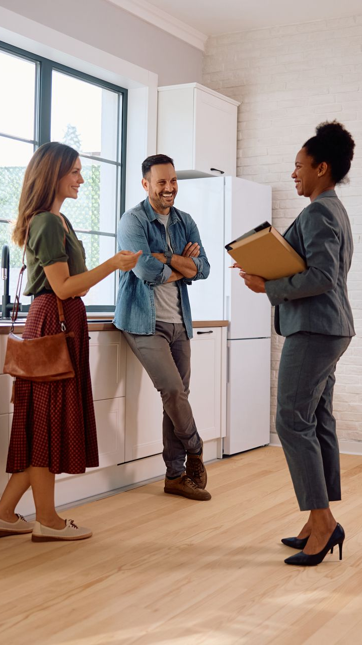A real estate agent showing a kitchen to a couple, the woman pointing.
