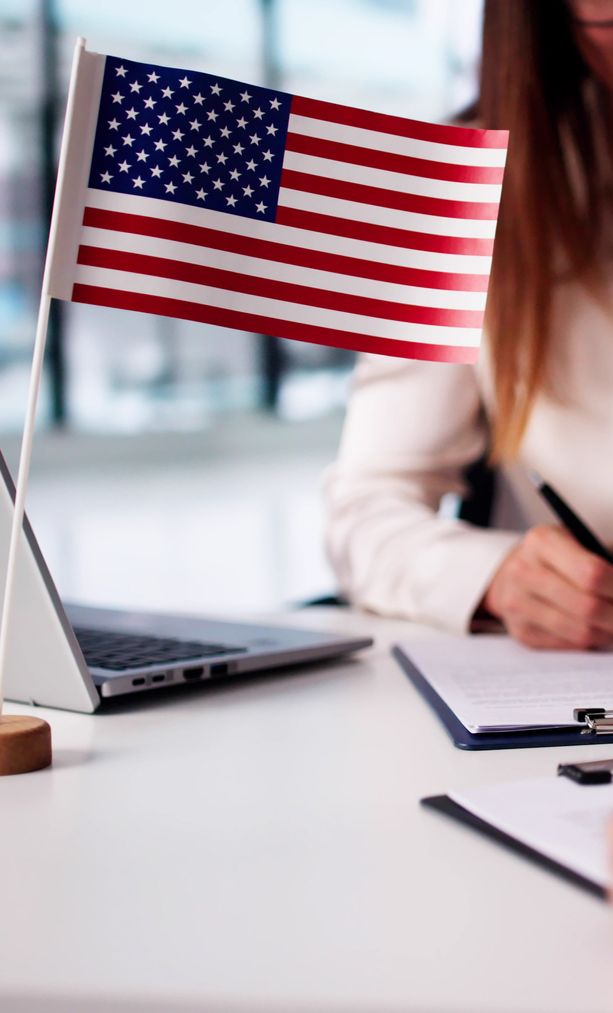 American flag on desk next to laptop and paperwork, a person is writing.