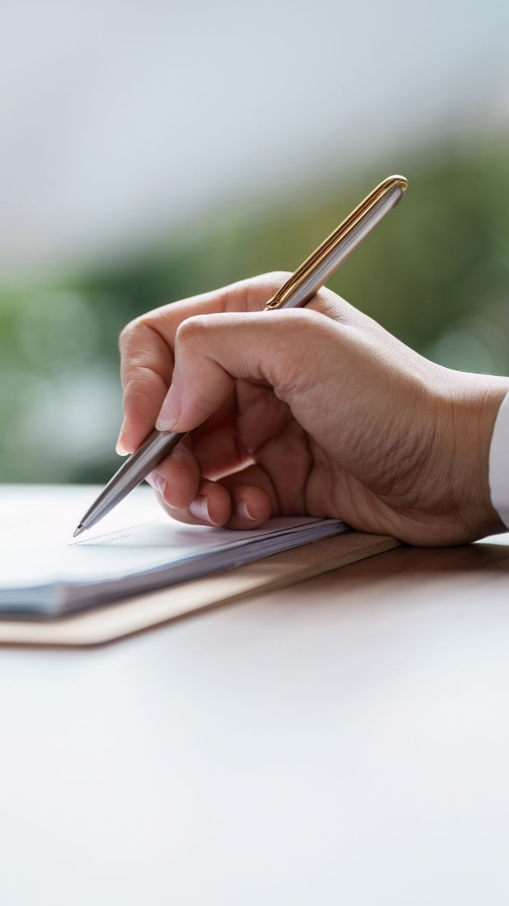 Hand writing on a paper on a desk. Silver pen in hand, focused.