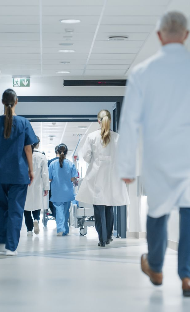 People, including medical staff, walk down a hospital hallway.