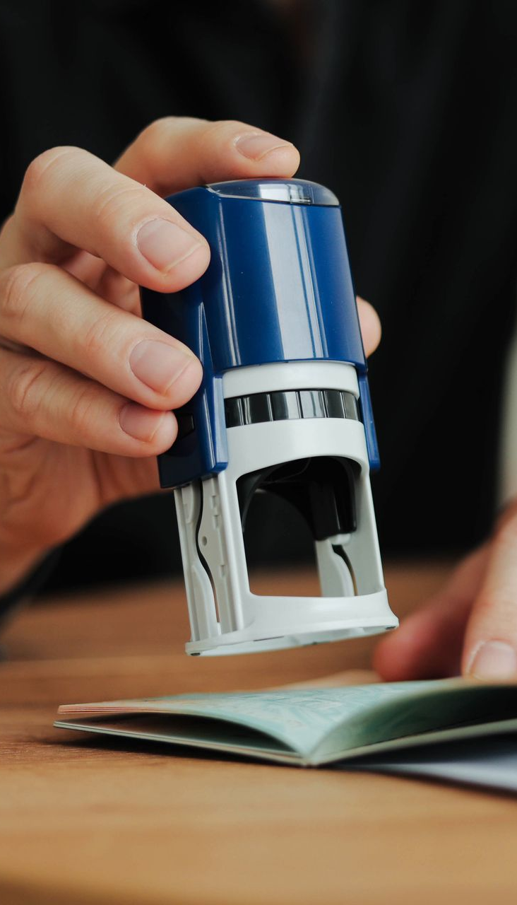 Person stamping a passport with a blue and white self-inking stamp on a wooden table.