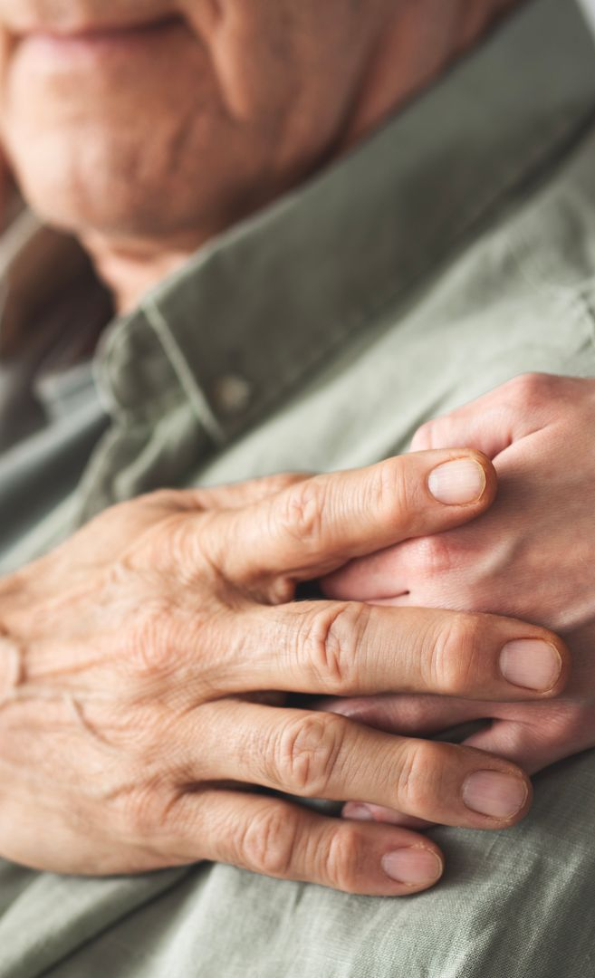 Two pairs of hands, one resting on the other. Older, wrinkled hands on top of younger hands; both resting on a shirt.