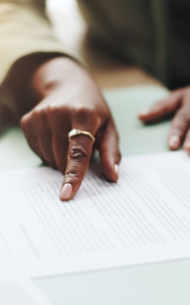 Hand pointing at text on a paper. The hand has a ring on a finger, with a blurred background.