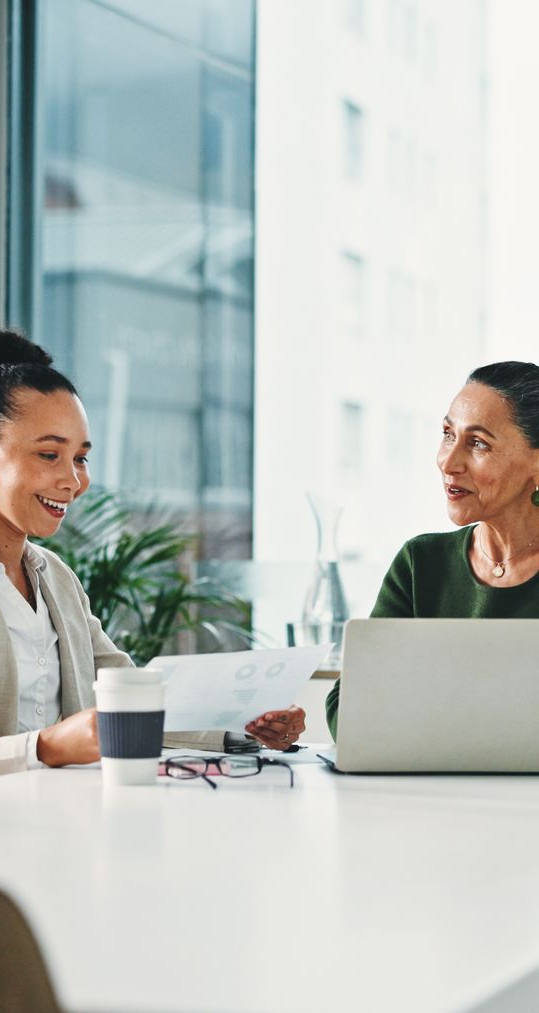 Two people at a table reviewing documents and a laptop, one smiling, in an office.