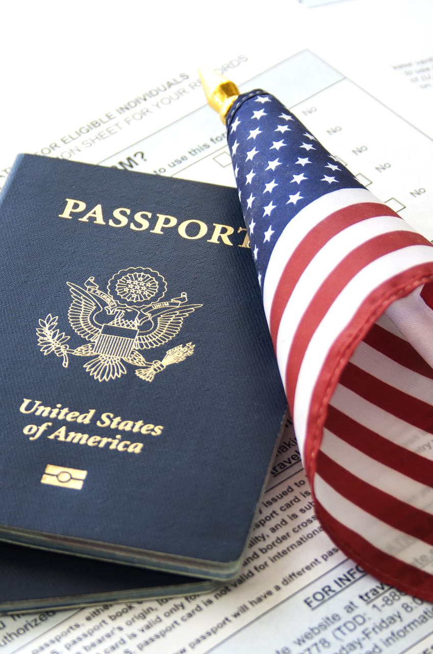United States passport and small American flag on top of paperwork.