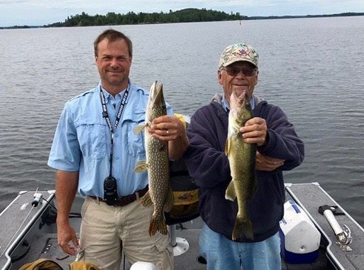 Two anglers on a boat holding up two fish on a calm lake
