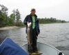 Person standing on a boat holding up a fish on a calm lake under an overcast sky