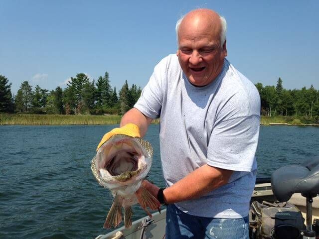 Man on a boat holding up a large fish over a lake on a sunny day