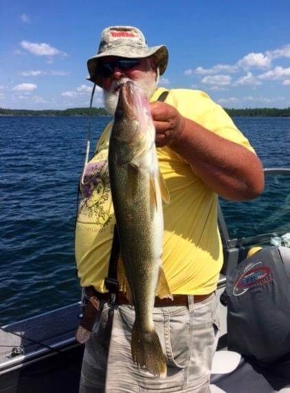 Person on a boat holding up a large fish on a sunny lake