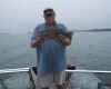 Man standing on a boat holding a large fish, with open water in the background