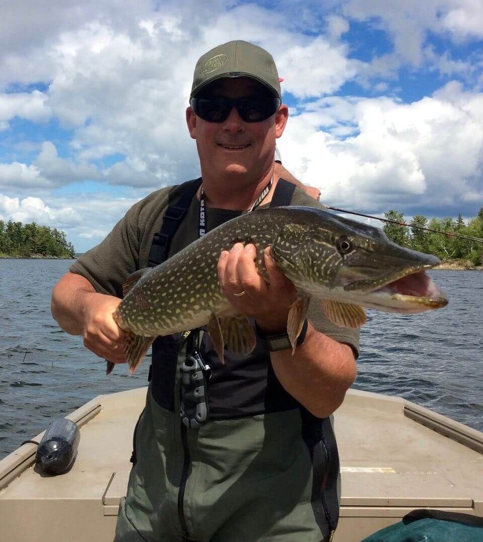 Person on a boat holding a large spotted fish on a lake under a cloudy sky