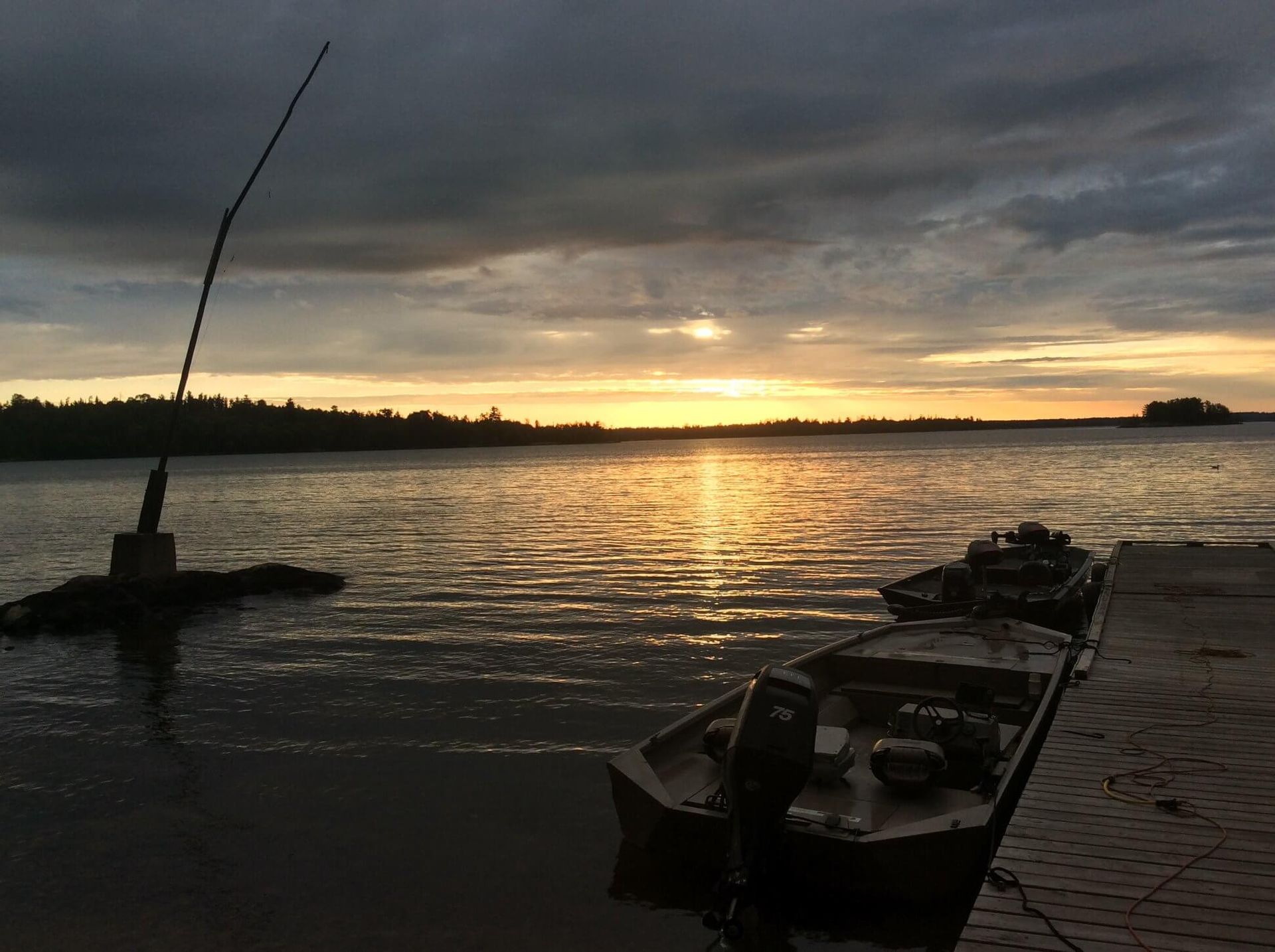 Sunset over a lake with silhouetted fishing rods and boats along the shore