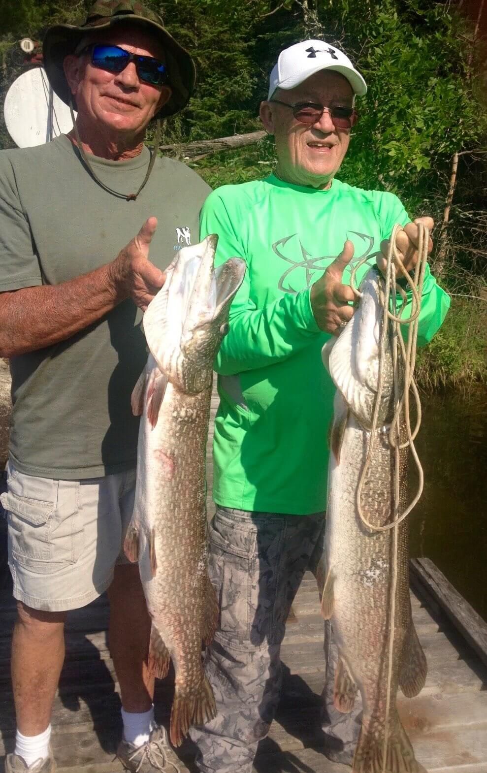 Two fishermen posing on a dock, each holding a large caught fish.