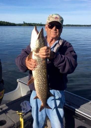 Person on a boat holding a large fish on a calm lake.