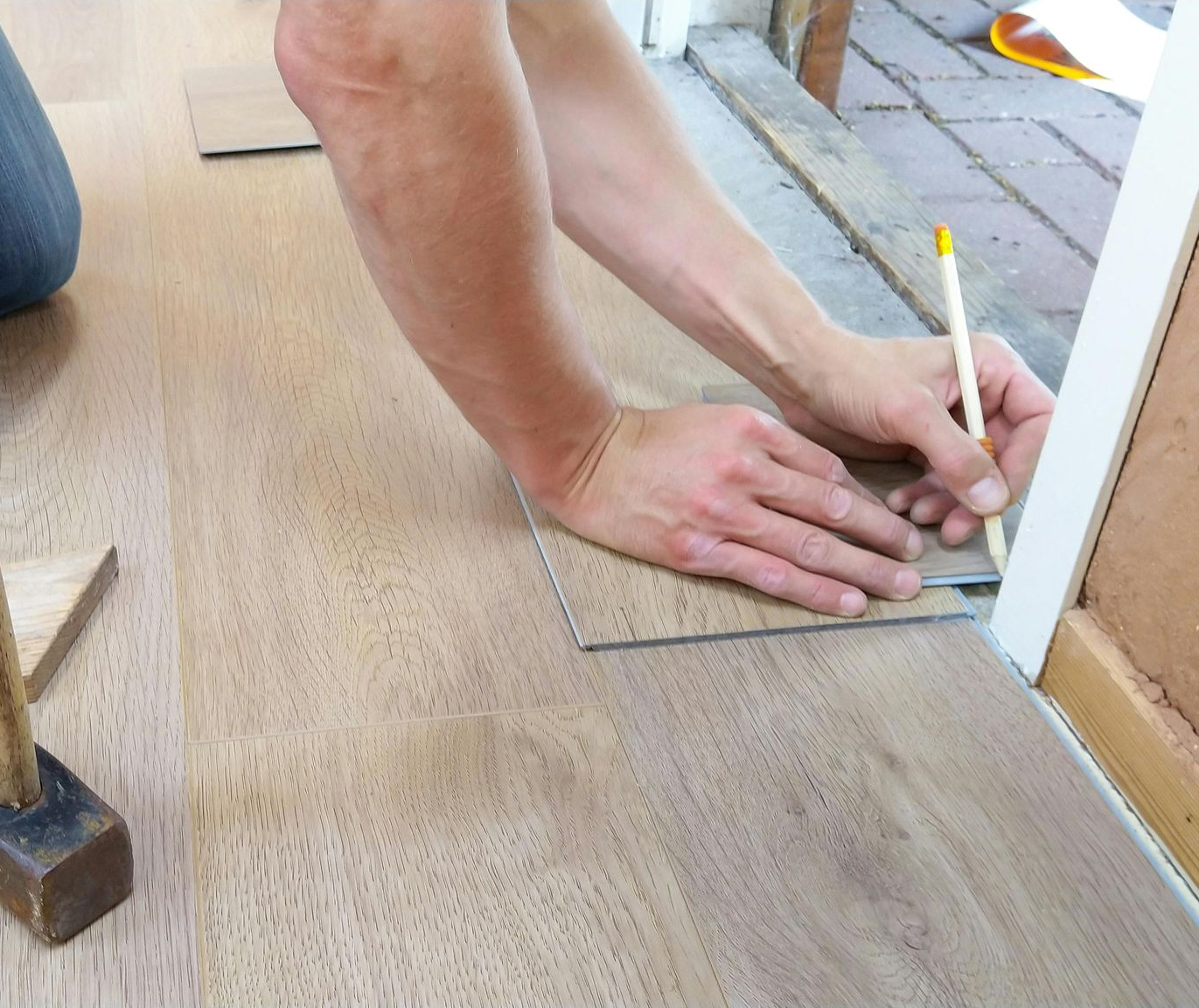 Person using a pencil and square to mark a flooring plank, near a doorway.