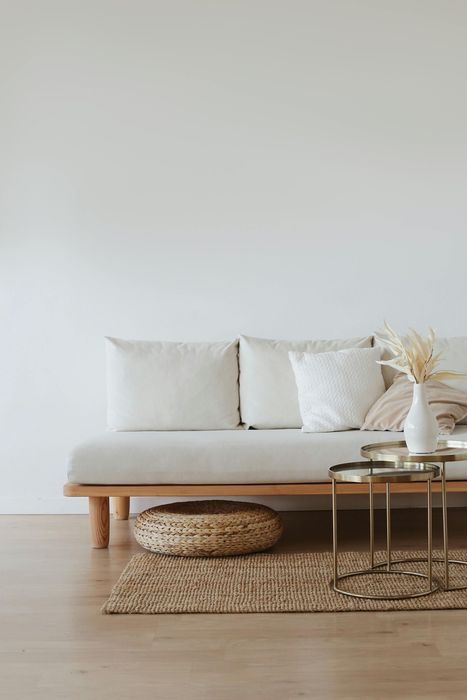 Neutral-toned living room with beige sofa, pillows, rug, and side tables; a decorative vase sits on one table.