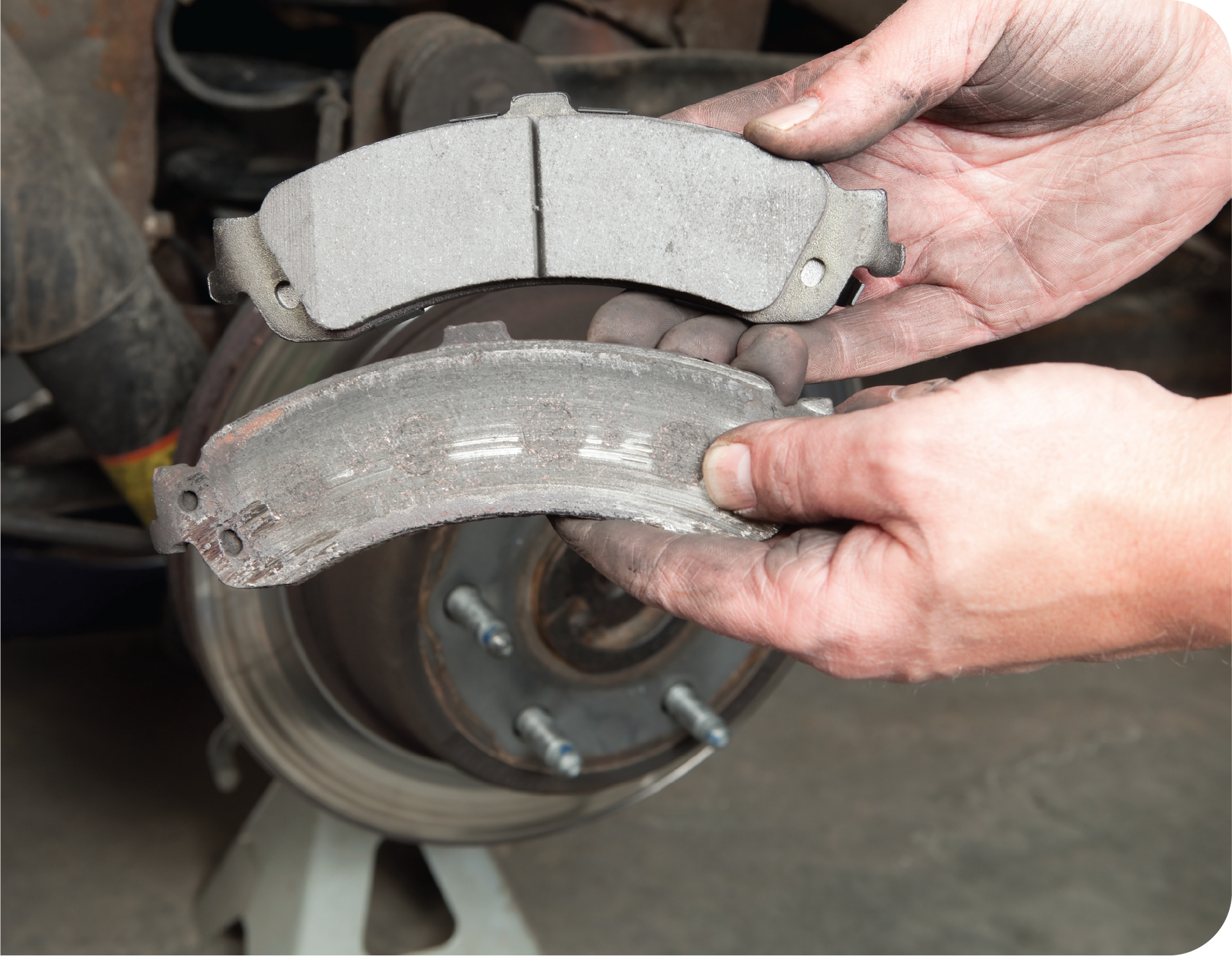 A person is holding a brake pad in front of a car.