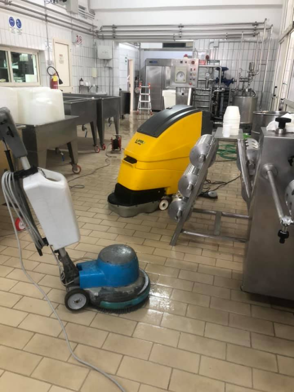 Persona con tuta protettiva che spruzza insetticida vicino a un mobiletto di legno in una stanza.