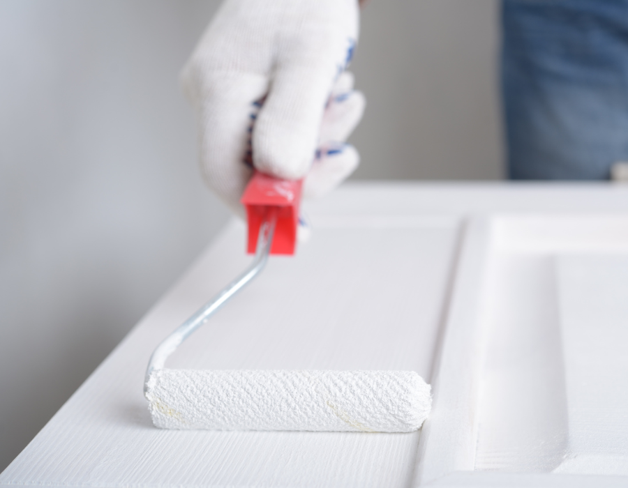 Persona che dipinge di bianco una porta con un rullo.