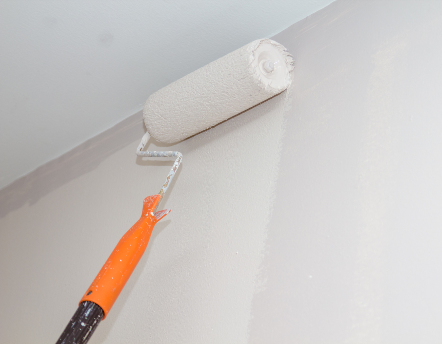 Rullo per applicare vernice bianca su una parete grigio chiaro.