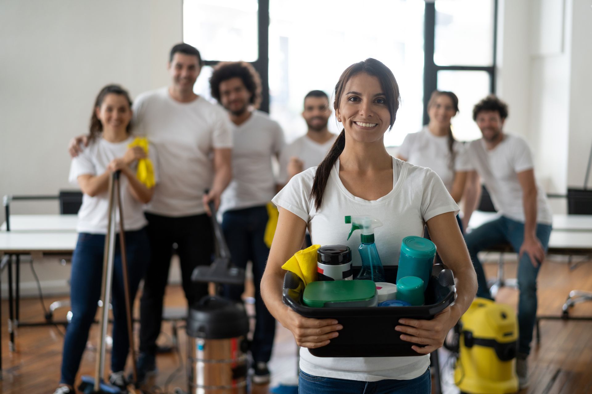 Un gruppo di persone in camicia bianca e jeans, sorridenti mentre tengono in mano prodotti per la pulizia in un ufficio.