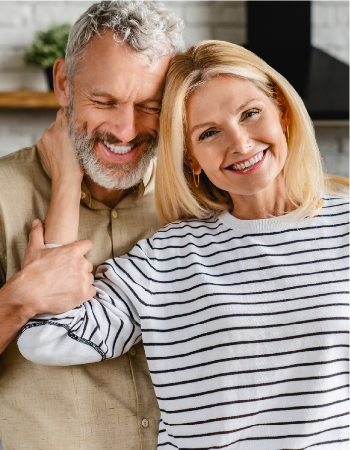 A man and a woman are hugging each other and smiling . the woman is wearing a striped shirt.