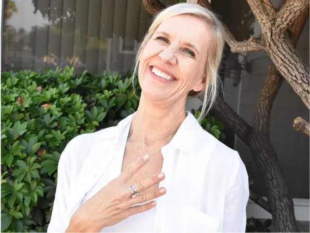 A woman in a white shirt is smiling in front of a tree.