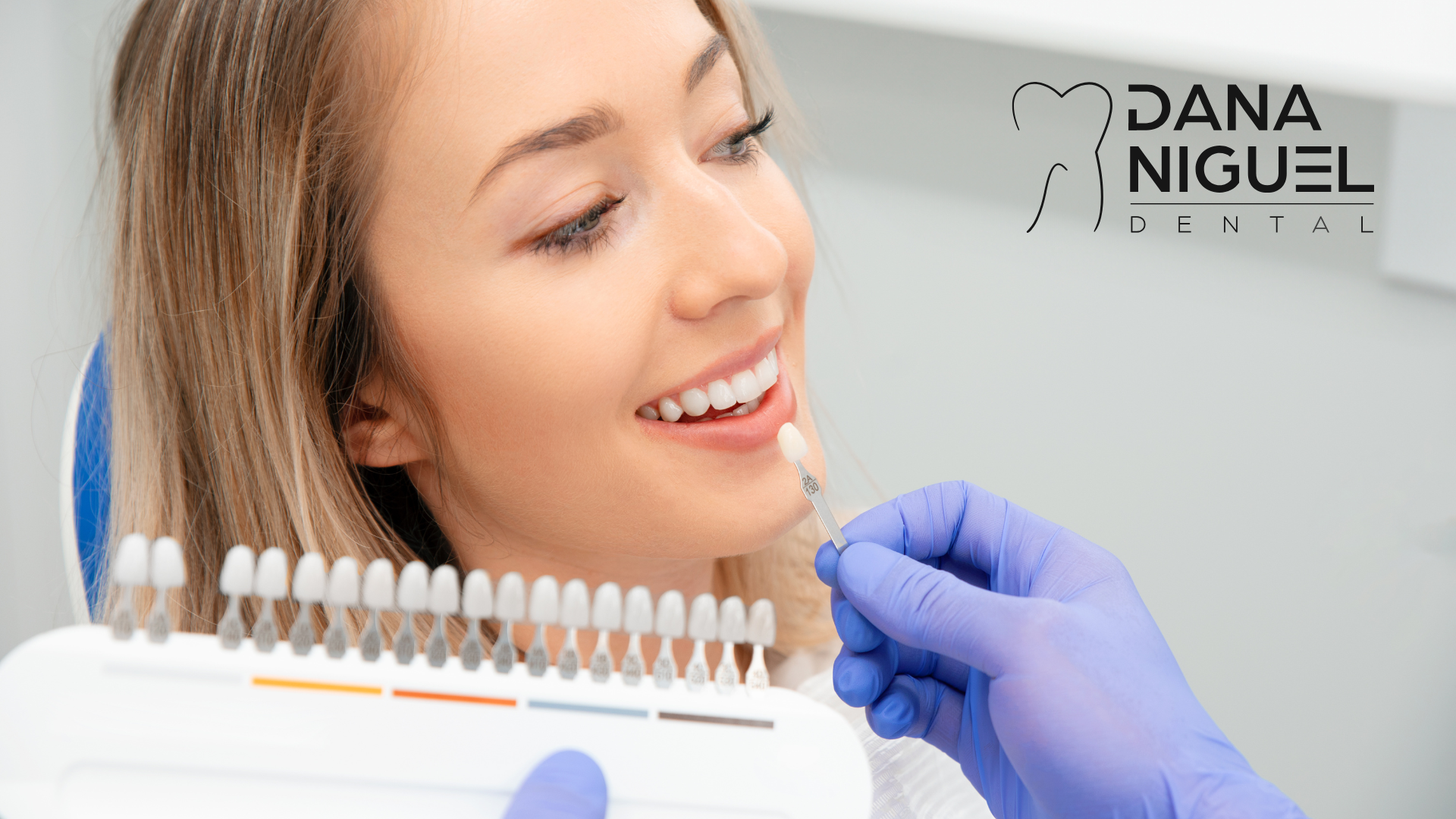 A woman is sitting in a dental chair while a dentist examines her teeth.