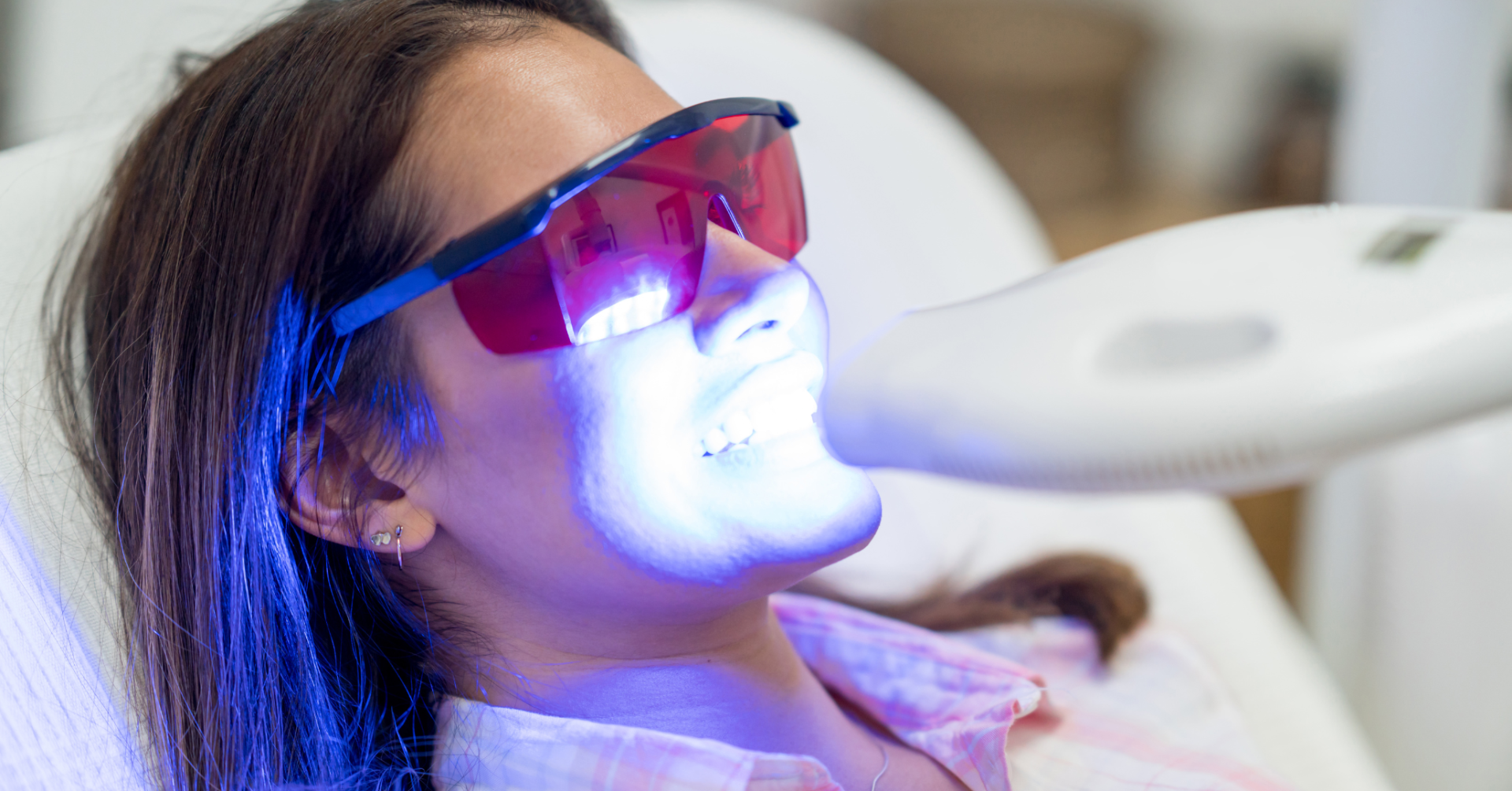 A woman is getting a teeth whitening treatment at a dental office.