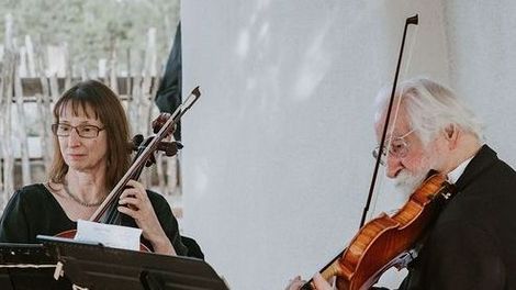 Rebecca Caron and Tomas Weber are sitting on a patio playing cello and violin.
