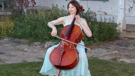 Rebecca Caron wearing a blue dress playing the cello outside