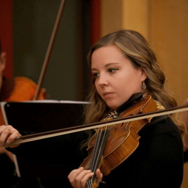 Young woman with dark blonde hair playing violin during a concert.