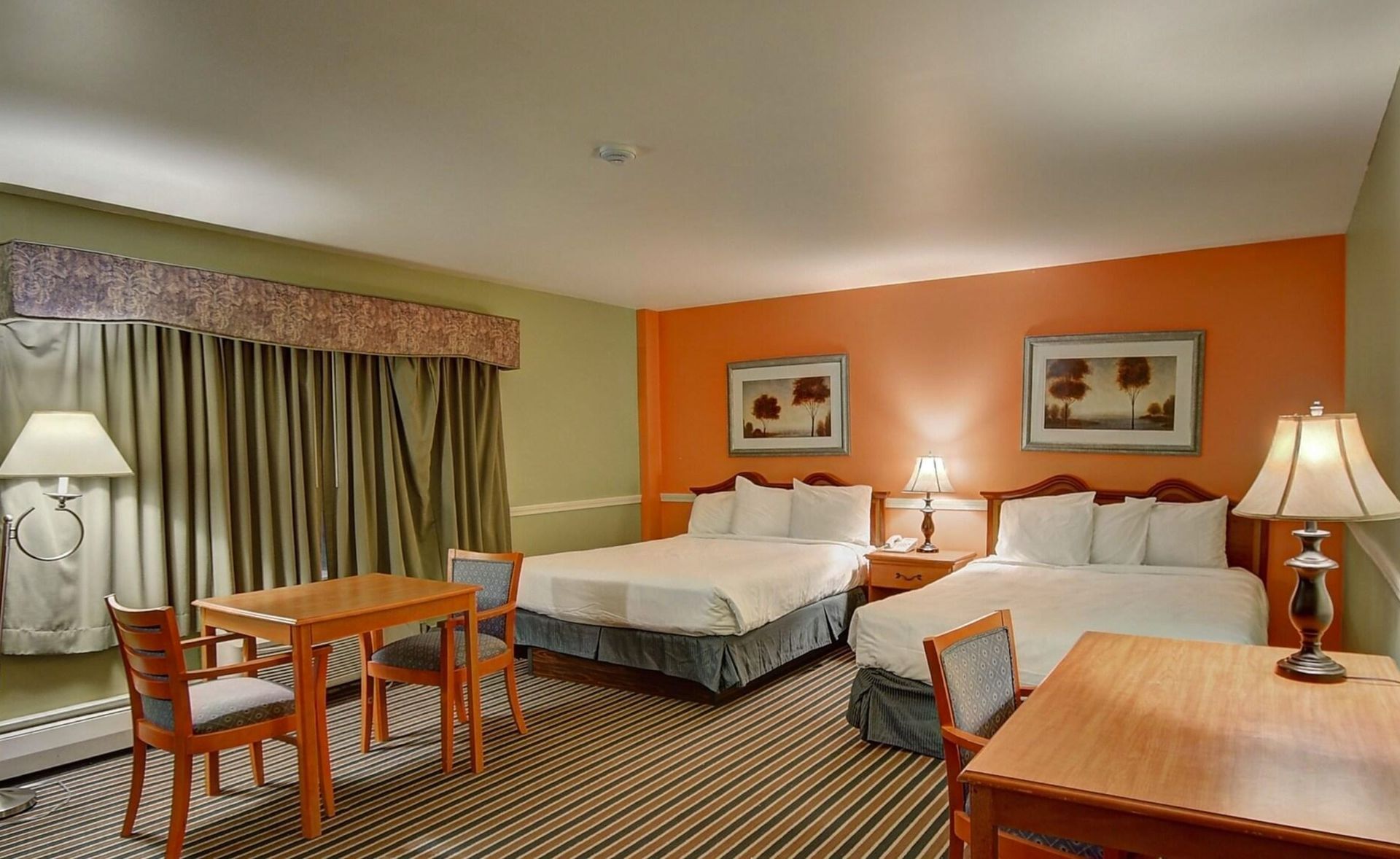 Hotel room with two double beds, desk, lamps, and orange accent wall